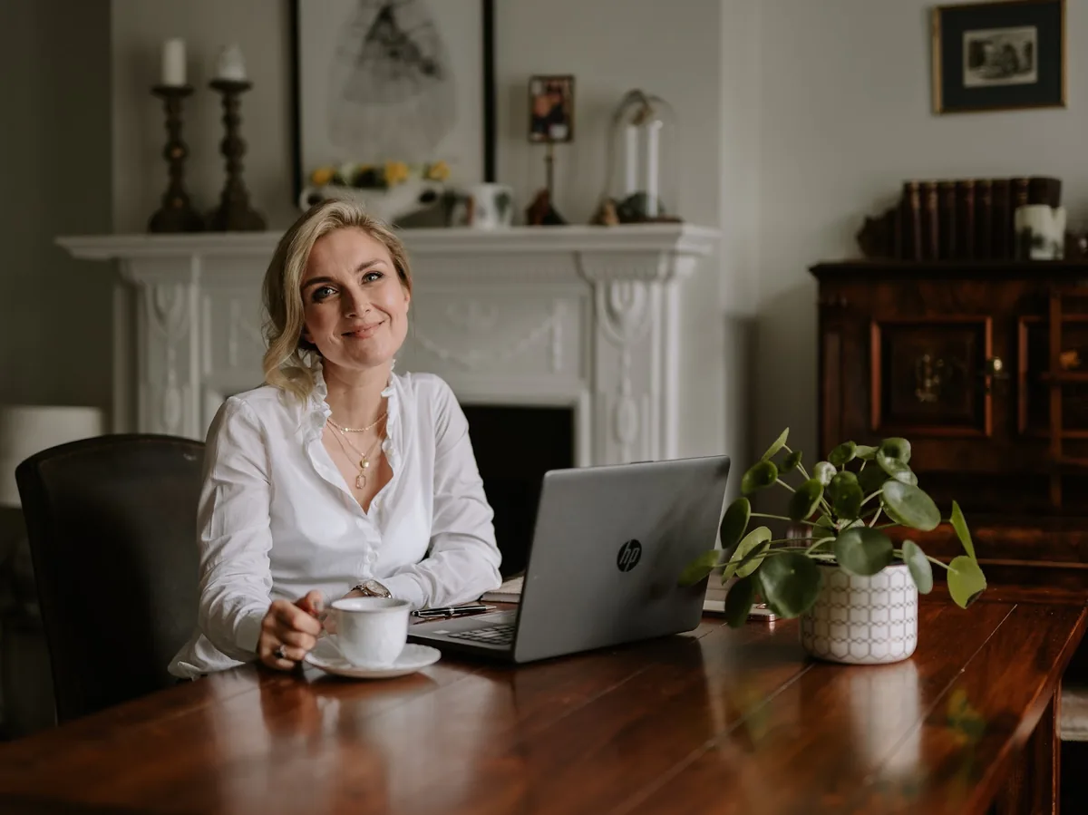 The stylist at her dining table with a laptop and coffee, planning a wedding booking
