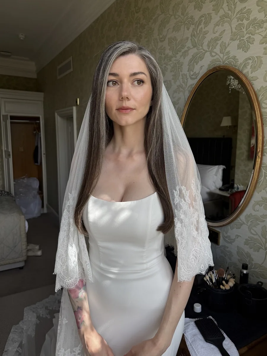 Bride in a satin gown and long lace-edged veil with full bridal makeup and soft waves