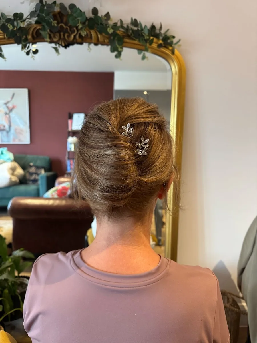 Sleek twisted updo finished with a pearl hairpin, seen in a mirror beside a eucalyptus garland