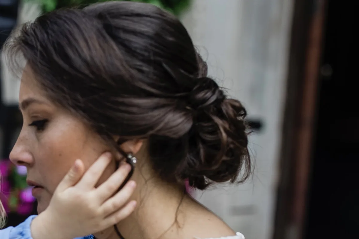 Side profile detail of a twisted bridal updo and a drop earring, hand raised to the ear
